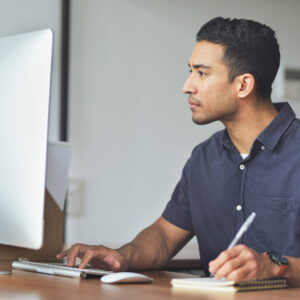 Online Courses man looking at computer screen and writing down notes